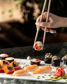 a person holding chopsticks above a plate of sushi and other food items