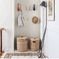 two baskets sit on the floor in front of a wall mounted coat rack with hats and utensils