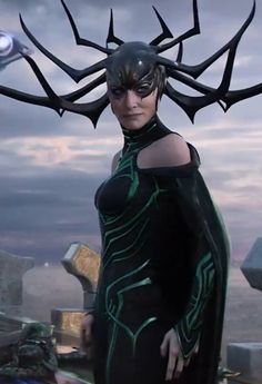 a woman dressed in black and green with horns on her head standing next to an alien like creature