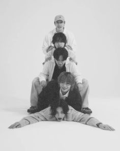 four people sitting on top of each other in front of a white background with one person standing