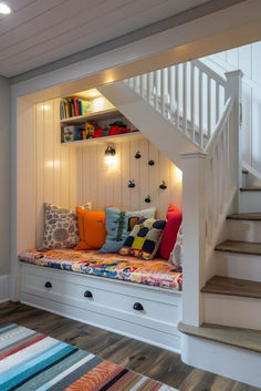 there is a bench with pillows on it under the stairs in this room that has built - in bookshelves