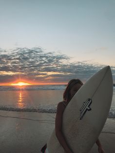 a woman carrying a surfboard on the beach at sunset