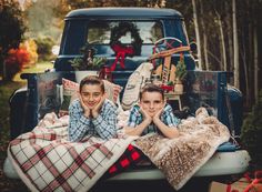 two young boys laying in the back of a pickup truck with christmas presents on the bed