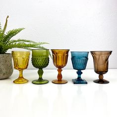 five different colored glass goblets sitting next to each other on a white table