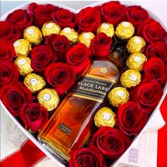 a heart shaped box filled with roses and chocolates next to a bottle of liquor