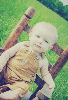 a baby sitting on top of a wooden chair in the middle of a grass field