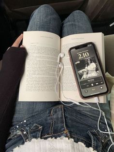 an open book sitting on top of a person's lap next to headphones