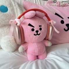 a pink teddy bear with headphones sitting on a bed