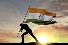 a man holding a flag on top of a hill with the sun in the background