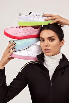 a woman holding five pairs of adidas sneakers on her head and looking at the camera