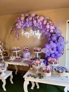 a table topped with lots of cakes and cupcakes next to a cake arch