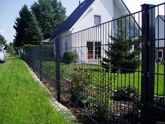 a white house behind a black fence in front of some trees and grass with a truck parked next to it