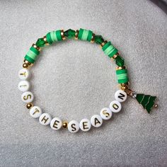 "The Tis The Season Christmas Beaded Word Bracelet was made using 6mm crystal bicone beads, circular spacer beads, and heishi clay beads. The words \"TIS THE SEASON\" are spelled out on white round letter beads in gold writing. A gold tone and green Christmas tree charm dangles from the bracelet. 🎄  Bracelets are all HANDMADE with love and care by myself, Candice Marie, and they are always limited edition and one-of-a-kind. ❤️ The bracelet is stretchy and stackable and looks great stacked with Adjustable Beaded Stretch Bracelet For Christmas, Holiday Jewelry With Letter Beads, Holiday Jewelry With Letter Round Beads, Holiday Jewelry With Round Letter Beads, Adjustable Beaded Christmas Bracelets, Adjustable Christmas Beaded Bracelets, Adjustable Green Bracelets For Holiday, Adjustable Colorful Beaded Bracelets For Christmas, Adjustable Bracelets With Round Beads For Holiday