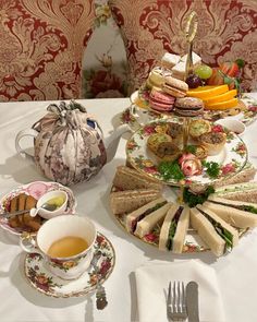 a table topped with plates and cups filled with food next to a tea pot on top of a white table cloth