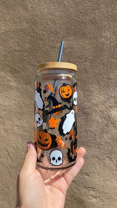 a hand holding a tumbler cup with halloween decorations on it and a straw in the cup