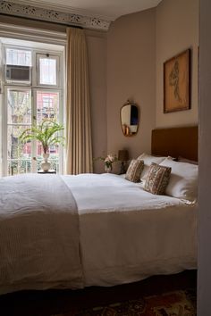 a bedroom with a large bed next to a window and potted plant in the corner