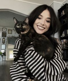 a woman holding a cat in her arms and smiling at the camera while wearing a striped shirt