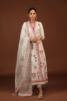 a woman wearing a white dress with pink trims and flowers on the bottom, standing in