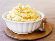 a white bowl filled with mashed potatoes on top of a wooden plate