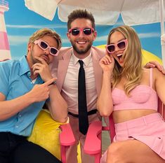 two men and a woman posing for a photo in front of a pink chair with an umbrella