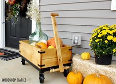 a wooden wagon filled with pumpkins and squash sitting on the front porch next to a potted plant