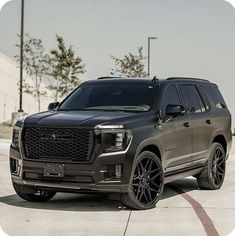 the front end of a gray suv parked on top of a cement parking lot with trees in the background