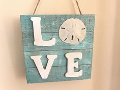 a wooden sign that says love with a sand dollar on it hanging from a wall