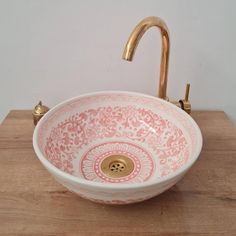 a pink and white bowl sink sitting on top of a wooden counter next to a faucet