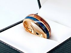 a gold ring with blue and brown wood in it sitting on top of a white box