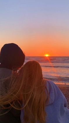 two people sitting on the beach watching the sunset