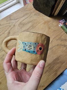 a hand holding a ceramic mug with a fish on it's side and a book in the background