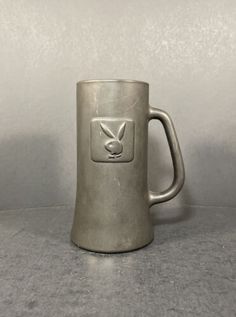 a metal mug sitting on top of a table next to a white wall and floor