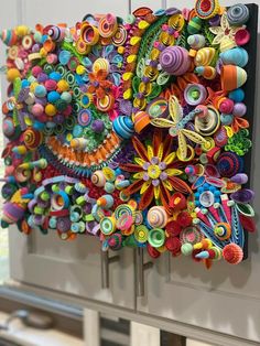 an art piece is hanging on the wall in front of a window with lots of colorful paper flowers