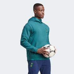 adidas 2023 LA Galaxy Travel Hoodie - Mystery Green Travelling for football can mean some cold temperatures. That's why the Galaxy pros are kitted out in this super cosy hoodie to stay ready for wherever the game takes them. Now you can too. Just throw your wallet in the snap-button kangaroo pocket, pull up the high collar and head out. An LA Galaxy badge and away-strip colours let you show your support anywhere. A minimum of 70% of this product is a blend of recycled and renewable materials. Re Adidas Sweatshirt For Sports Events In Winter, Adidas Sweatshirt For Winter Sports Events, Adidas Winter Sweatshirt For Sports Events, Green Adidas Sweatshirt For Winter, Urban Green Hoodie With Kangaroo Pocket, Green Urban Hoodie With Kangaroo Pocket, Green Outdoor Sweatshirt With Adjustable Hood, Sporty Sweat-resistant Outdoor Hoodie, Green Moisture-wicking Hoodie For Outdoor