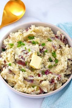 a bowl filled with mashed potatoes topped with butter and green onions next to a spoon