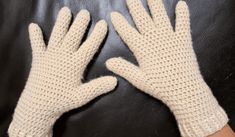 a pair of white knitted gloves sitting on top of a black leather couch