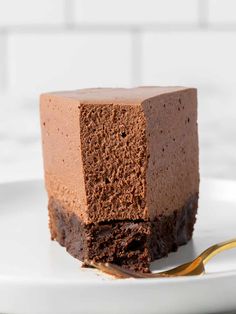 a piece of chocolate cake on a white plate with a gold fork in the foreground