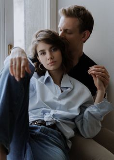 a man and woman sitting next to each other on a couch in front of a window