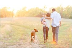 a man and woman walking down a dirt road with a baby in their arms as the sun sets behind them