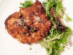 a white plate topped with two pieces of fried chicken next to a green leafy salad