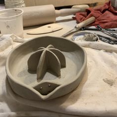 a white bowl sitting on top of a table covered in pottery and other crafting supplies