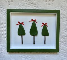 three green christmas trees in a shadow box with red ribbon on them, hanging from the wall