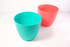 two different colored cups sitting next to each other on a white surface, one is blue and the other is pink