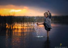 a little boy standing in the water splashing with his feet up and arms out