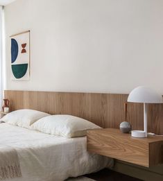 a bed with white sheets and pillows next to a wooden headboard in a bedroom