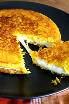 a pancake with one slice missing from it on a black plate, sitting on a wooden table