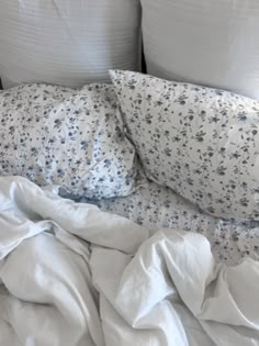 an unmade bed with white linens and blue flowers on the pillowcase is shown