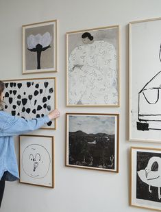 a woman standing in front of a wall with many paintings hanging on it's side