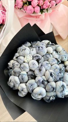 a bouquet of pink roses and blue shells in a black paper wrapper on a table