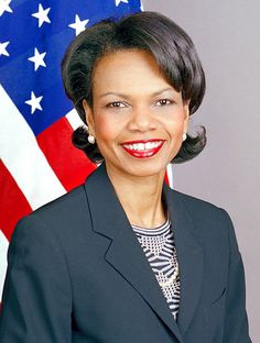 a woman standing in front of an american flag and wearing a suit with her hair pulled back